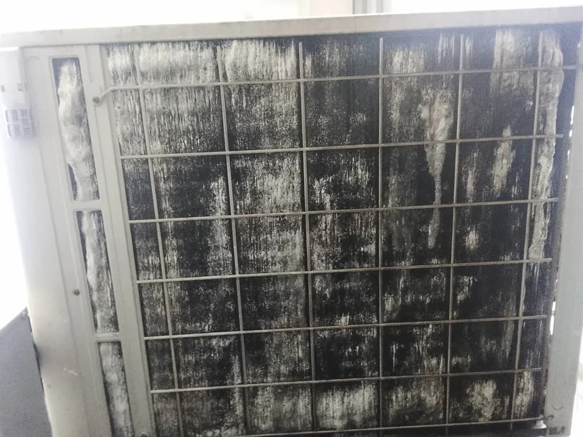 Outdoor aircon condenser coil coated in black grime and white streaks
